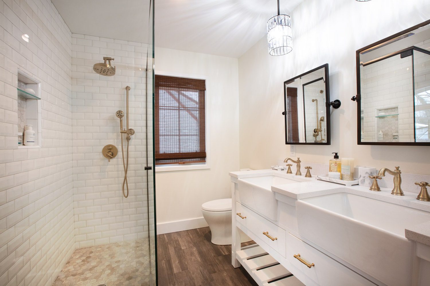 Long remodeled bathroom. A large tiled walkin shower is featured on the left of the photo. across from a double vanity featuring large farm house sinks