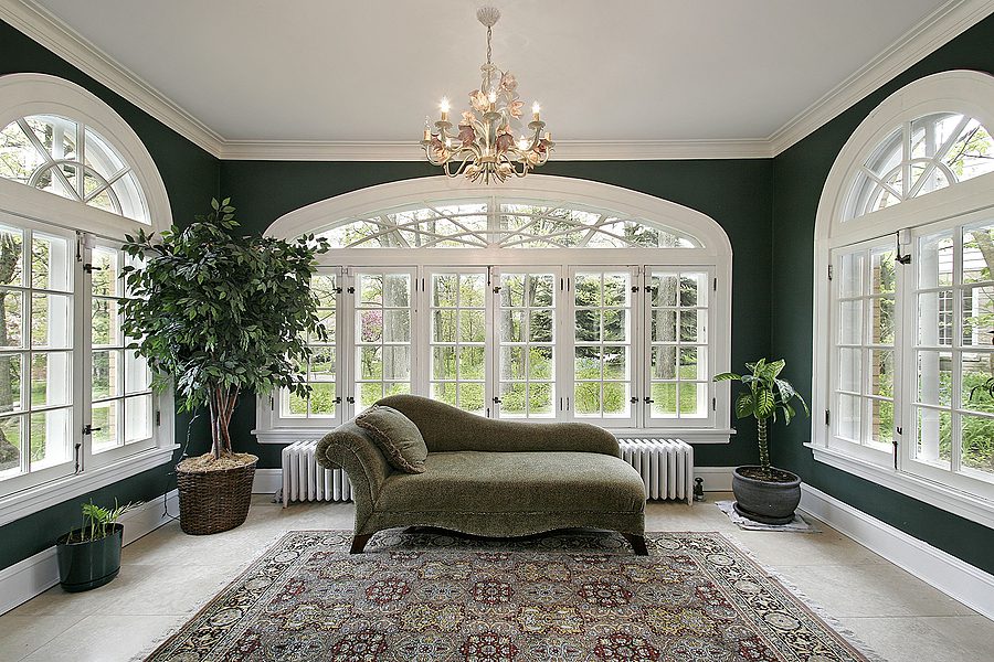 Four-season room with dark green walls, a sofa, area rug and a large window.