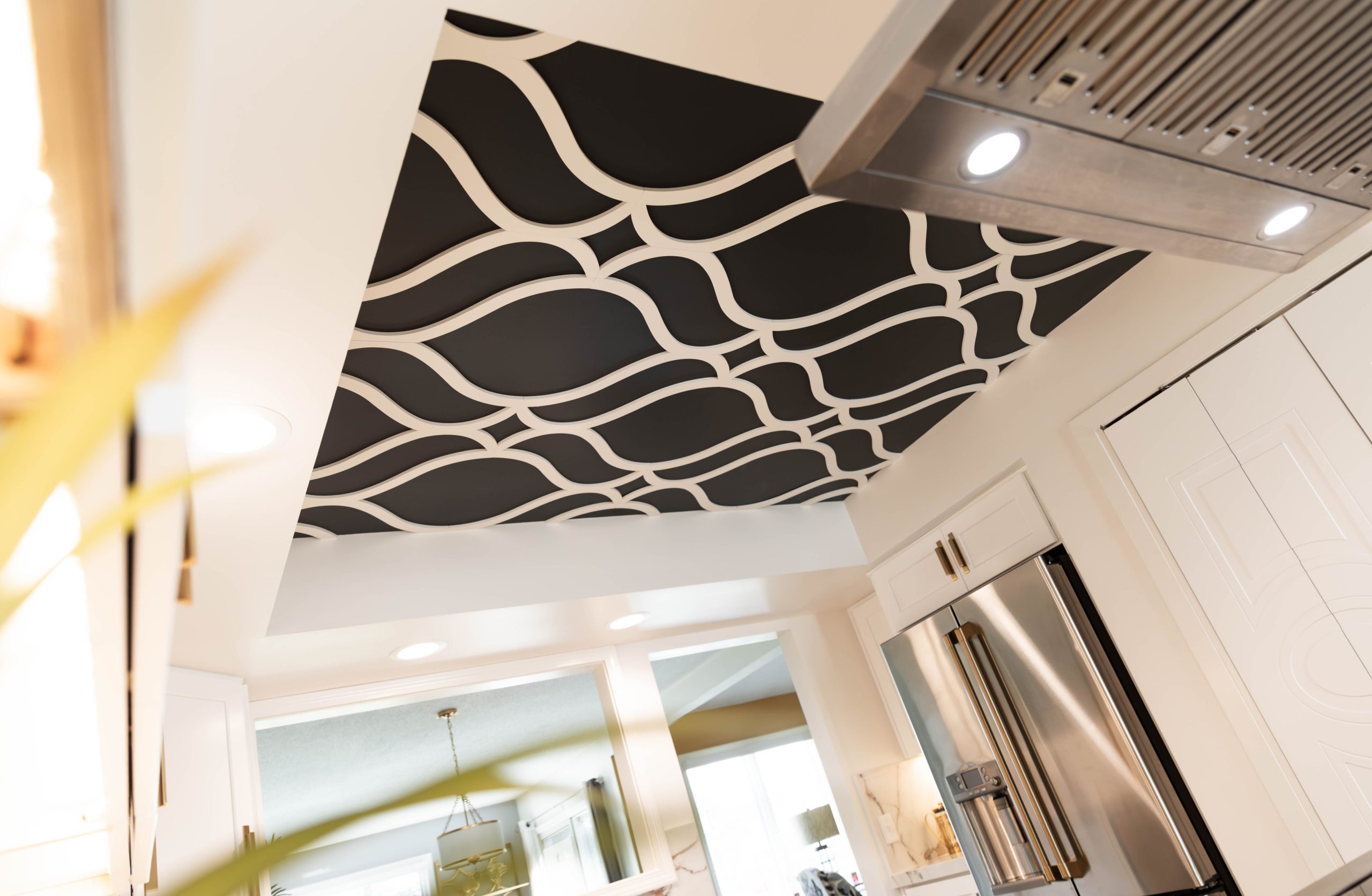 Kitchen ceiling features a bold black-and-white wavy pattern panel above white cabinets and stainless steel appliances in a modern kitchen.